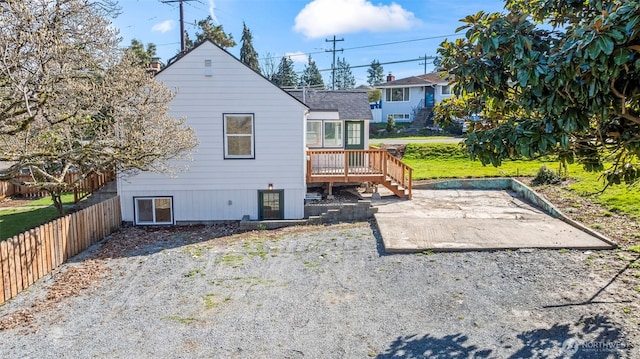 rear view of house with a shingled roof, fence, a wooden deck, and a patio