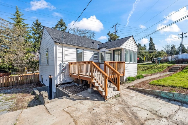 rear view of property featuring a shingled roof, fence, and a wooden deck