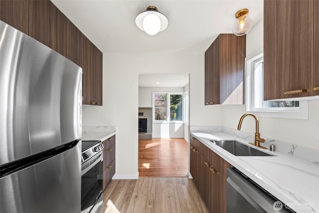 kitchen with light wood-style flooring, a sink, appliances with stainless steel finishes, light stone countertops, and modern cabinets