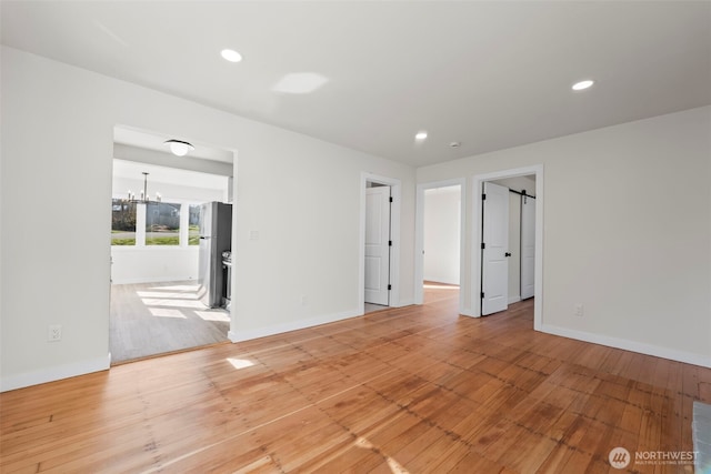 spare room with recessed lighting, light wood-style flooring, baseboards, and an inviting chandelier