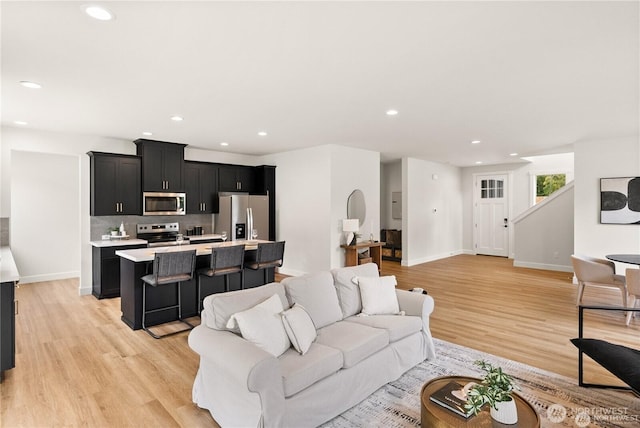 living area featuring light wood-type flooring, stairway, baseboards, and recessed lighting