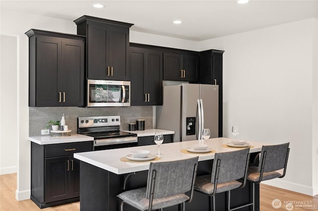 kitchen featuring stainless steel appliances, a kitchen breakfast bar, light countertops, tasteful backsplash, and a center island with sink