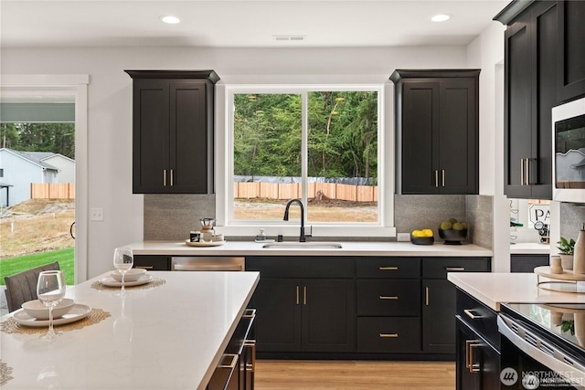 kitchen with a sink, light countertops, dark cabinetry, light wood finished floors, and tasteful backsplash