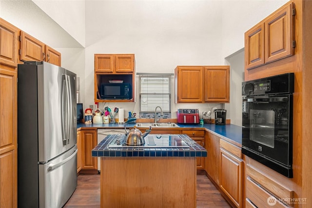 kitchen featuring tile counters, a kitchen island, dark wood-style flooring, black appliances, and a sink