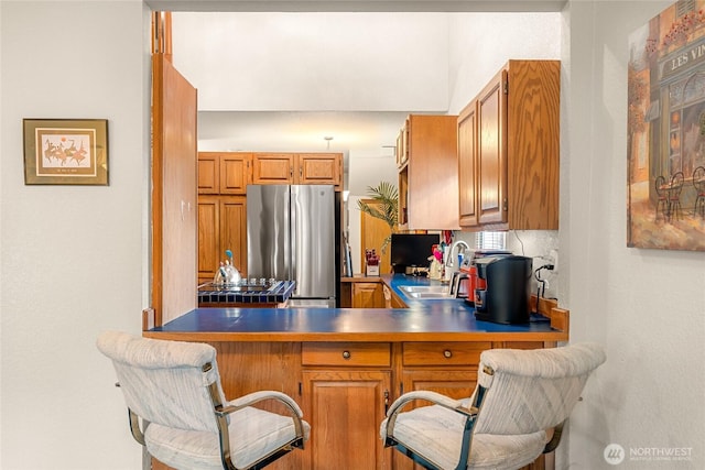 kitchen featuring a breakfast bar area, brown cabinetry, freestanding refrigerator, a sink, and a peninsula