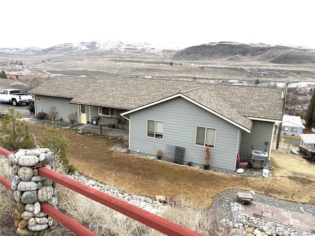 rear view of house featuring a shingled roof, central AC unit, and a mountain view