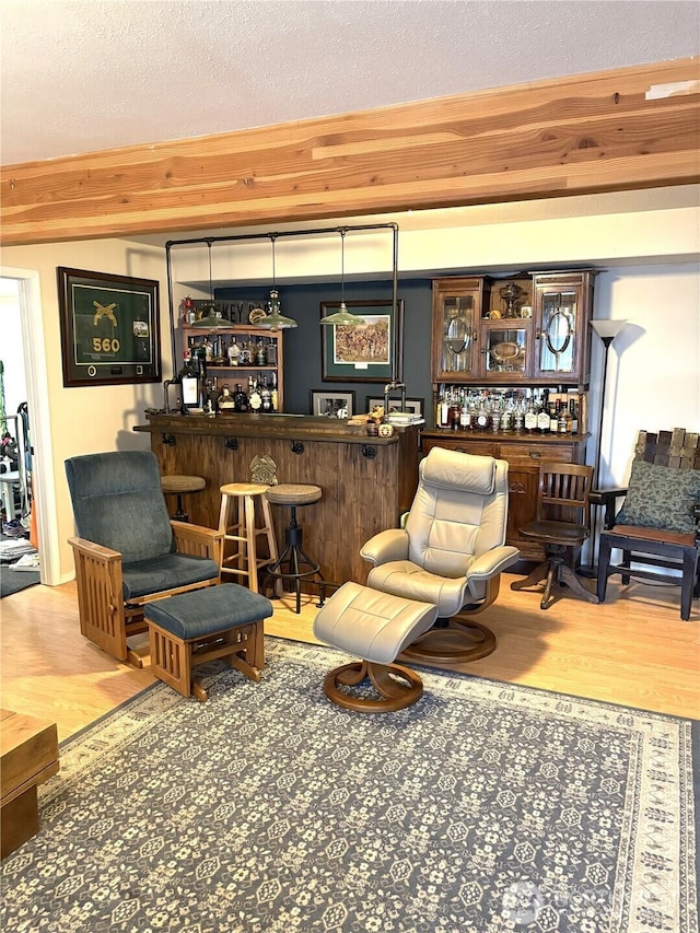 living area with a bar, a textured ceiling, wood finished floors, and beamed ceiling