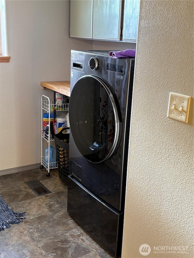 clothes washing area featuring a textured wall, visible vents, baseboards, cabinet space, and washer / clothes dryer