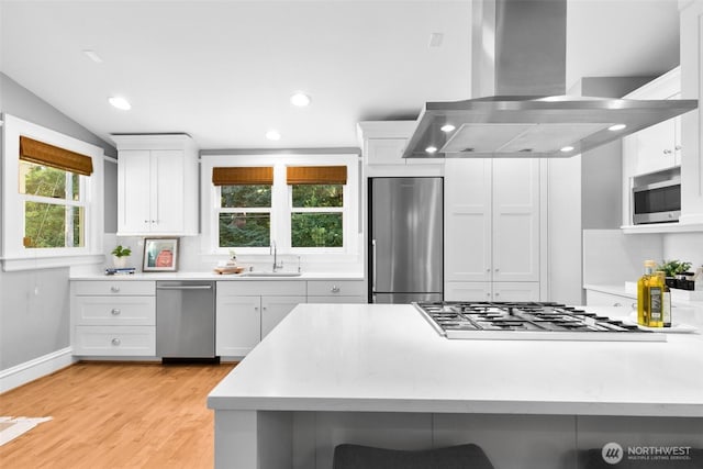 kitchen featuring a breakfast bar, light countertops, appliances with stainless steel finishes, a sink, and island range hood