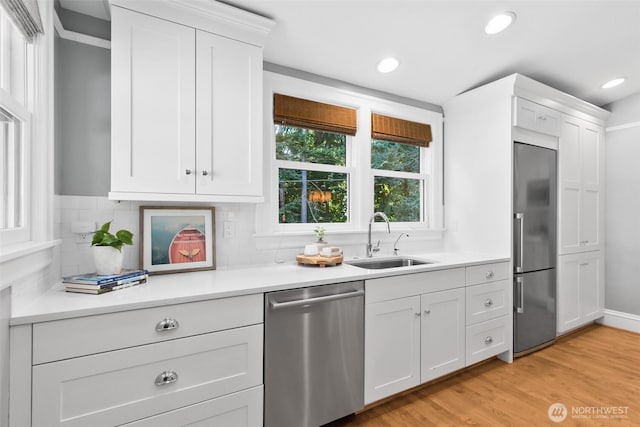 kitchen with stainless steel appliances, light countertops, light wood-type flooring, white cabinetry, and a sink