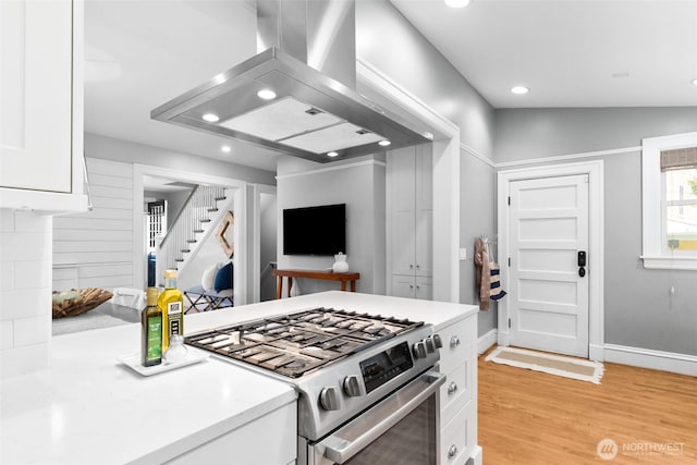 kitchen with open floor plan, island exhaust hood, light countertops, white cabinetry, and gas stove