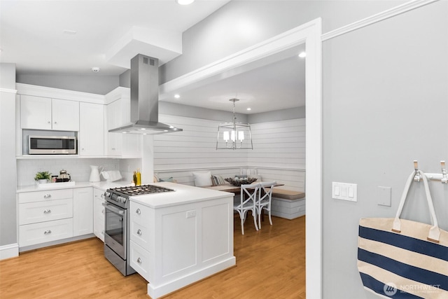 kitchen with island exhaust hood, stainless steel appliances, light countertops, white cabinetry, and light wood-type flooring