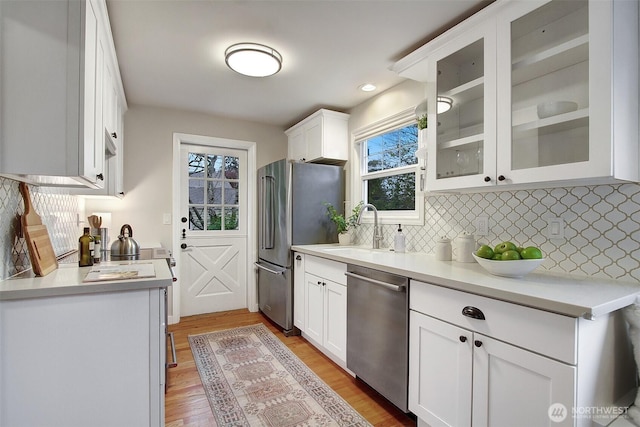 kitchen featuring glass insert cabinets, stainless steel appliances, light countertops, white cabinetry, and a sink