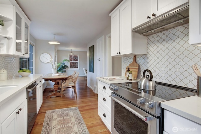 kitchen featuring under cabinet range hood, stainless steel appliances, white cabinets, light countertops, and glass insert cabinets