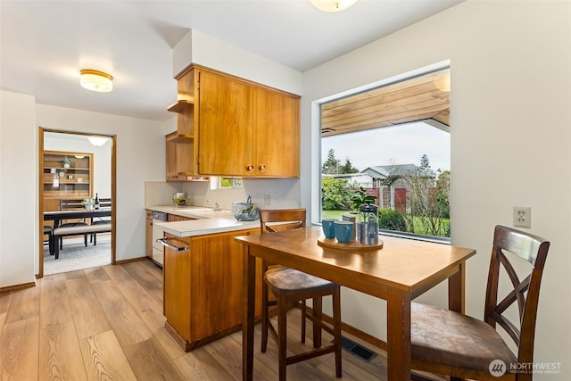 kitchen featuring open shelves, light countertops, light wood-style floors, white dishwasher, and a sink