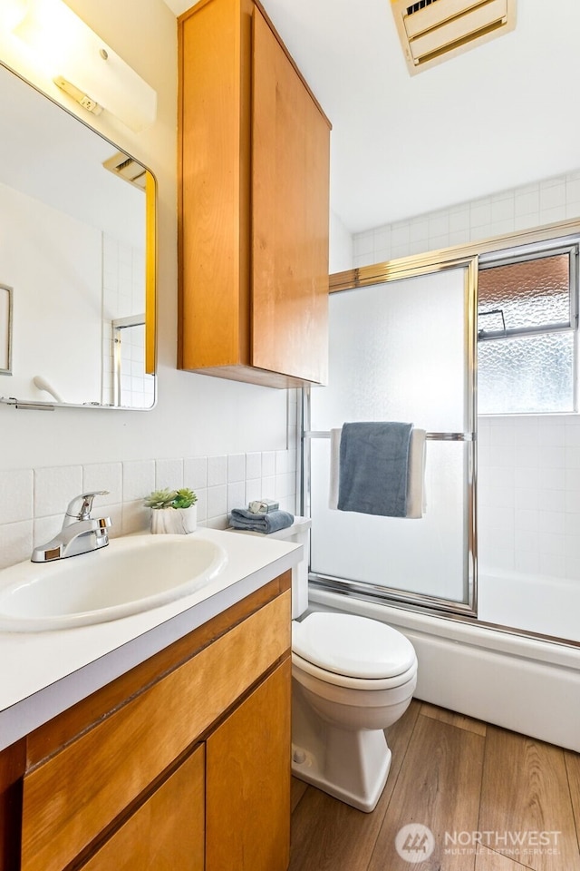 full bath featuring vanity, wood finished floors, visible vents, toilet, and combined bath / shower with glass door