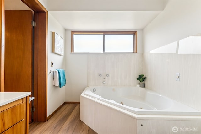 bathroom with a tub with jets, vanity, baseboards, and wood finished floors