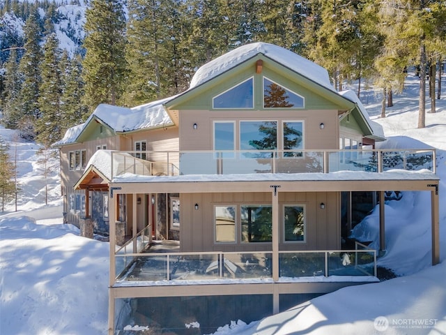 snow covered rear of property featuring a balcony and board and batten siding