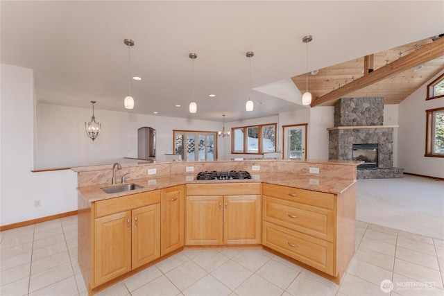 kitchen with a fireplace, stainless steel gas stovetop, open floor plan, a sink, and light stone countertops