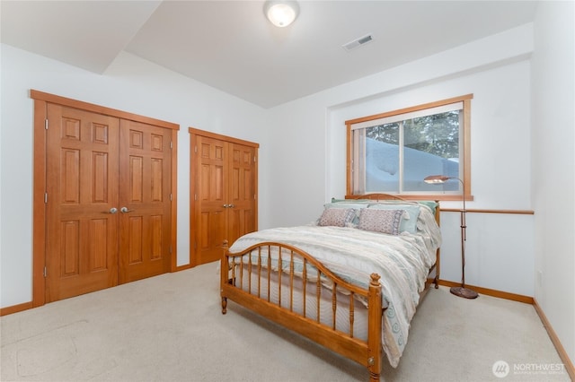 carpeted bedroom featuring multiple closets, visible vents, and baseboards