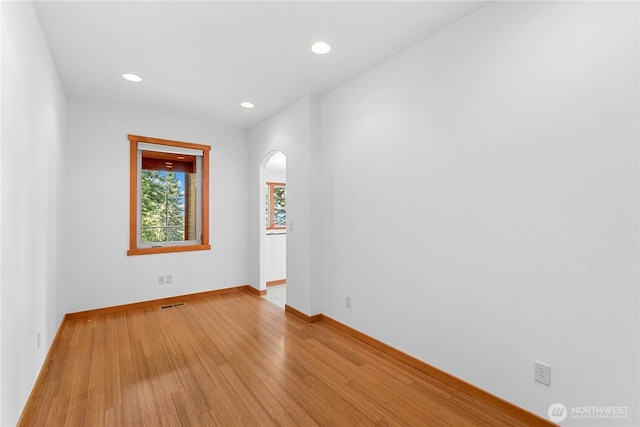 spare room featuring arched walkways, recessed lighting, light wood-style flooring, and baseboards