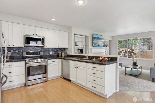 kitchen featuring decorative backsplash, appliances with stainless steel finishes, a peninsula, white cabinetry, and a sink