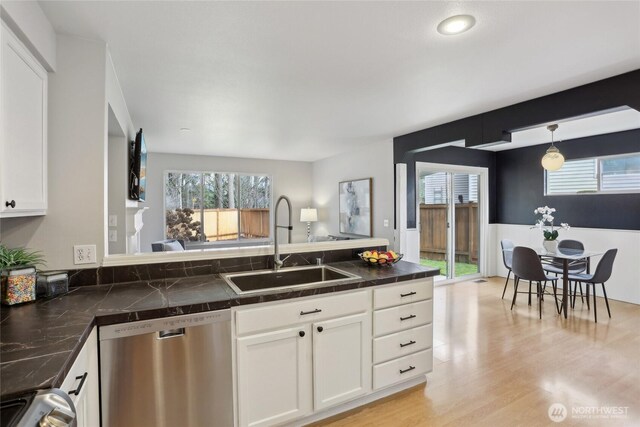 kitchen featuring white cabinets, light wood-style flooring, a peninsula, stainless steel dishwasher, and a sink