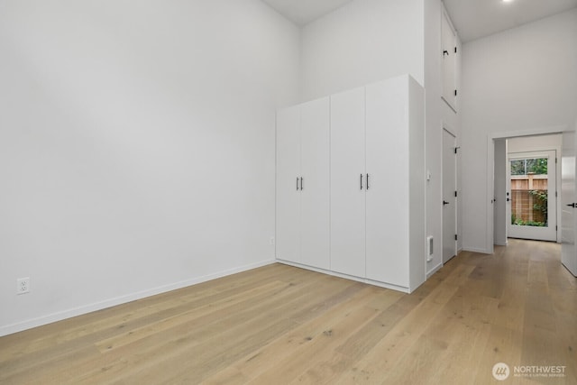 unfurnished bedroom featuring a towering ceiling, light wood-type flooring, and baseboards