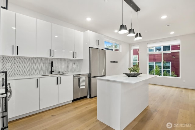 kitchen featuring stainless steel appliances, a sink, white cabinetry, hanging light fixtures, and light countertops