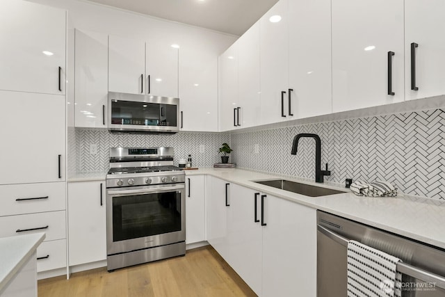 kitchen with stainless steel appliances, light countertops, light wood-style floors, white cabinetry, and a sink