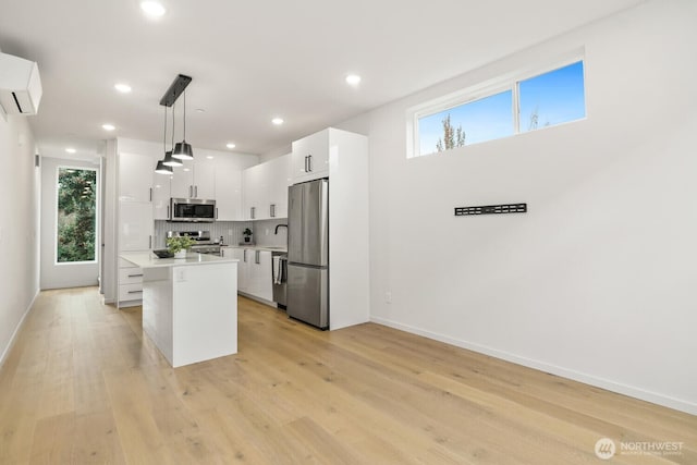 kitchen featuring a center island, stainless steel appliances, light countertops, hanging light fixtures, and white cabinetry