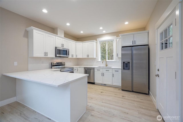 kitchen with white cabinets, a peninsula, a sink, light stone countertops, and appliances with stainless steel finishes