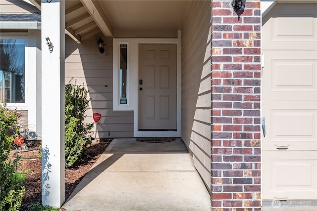 entrance to property featuring a garage and brick siding