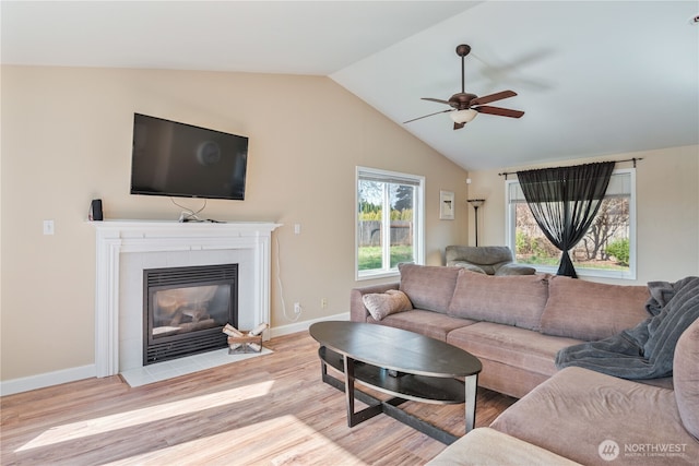 living room with light wood-type flooring, a fireplace, baseboards, ceiling fan, and vaulted ceiling