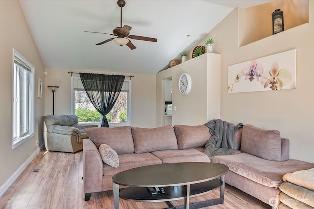 living area with baseboards, visible vents, light wood-style flooring, ceiling fan, and vaulted ceiling