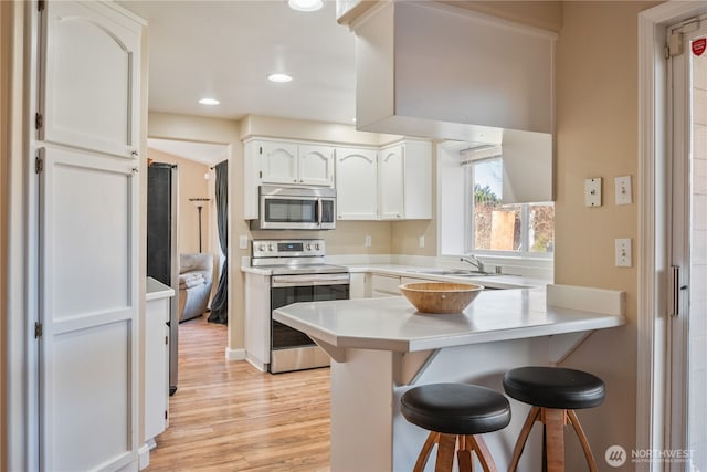 kitchen with light wood finished floors, white cabinetry, a breakfast bar area, a peninsula, and stainless steel appliances