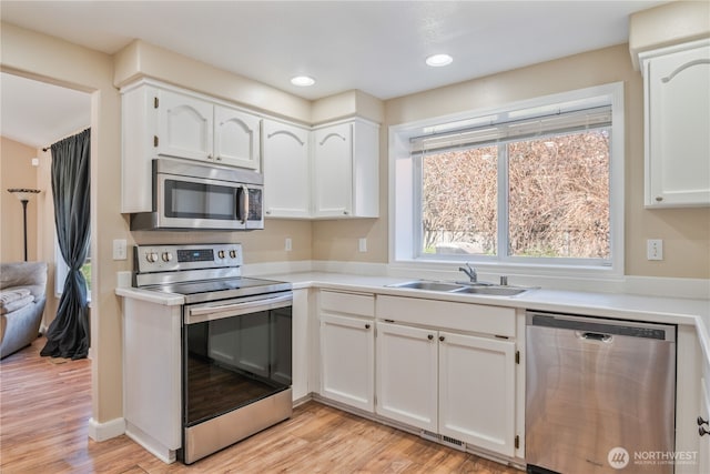 kitchen with light wood-style flooring, a sink, stainless steel appliances, light countertops, and white cabinets