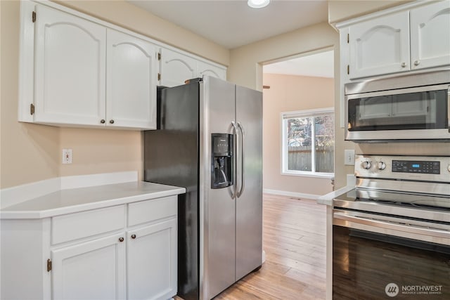 kitchen with light wood finished floors, baseboards, light countertops, appliances with stainless steel finishes, and white cabinetry