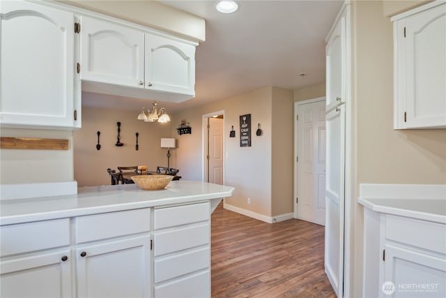 kitchen featuring wood finished floors, a peninsula, white cabinets, light countertops, and baseboards