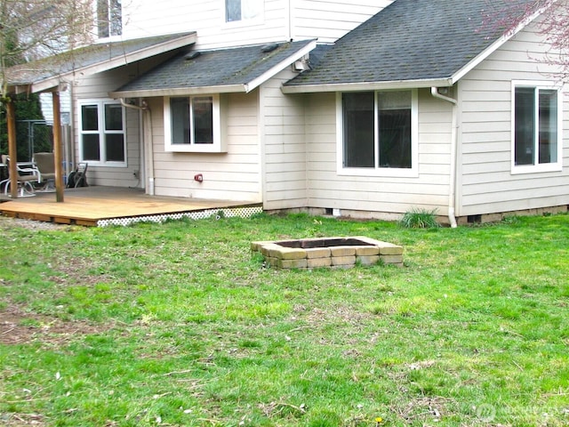 back of property with a yard, an outdoor fire pit, a deck, and a shingled roof