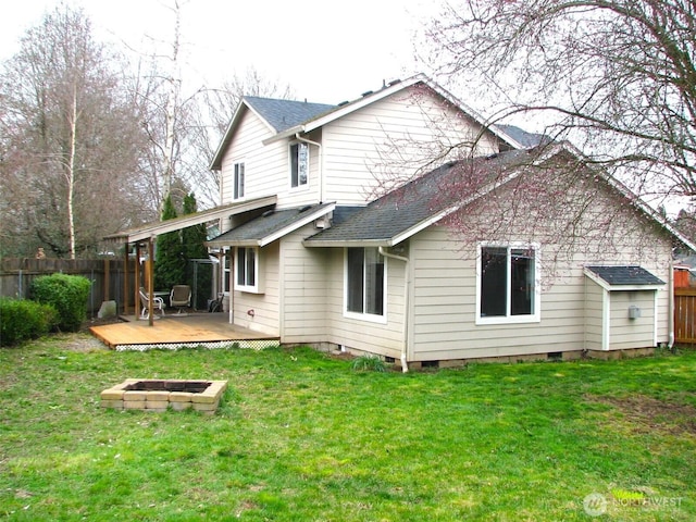 rear view of house with fence, roof with shingles, a wooden deck, an outdoor fire pit, and a lawn