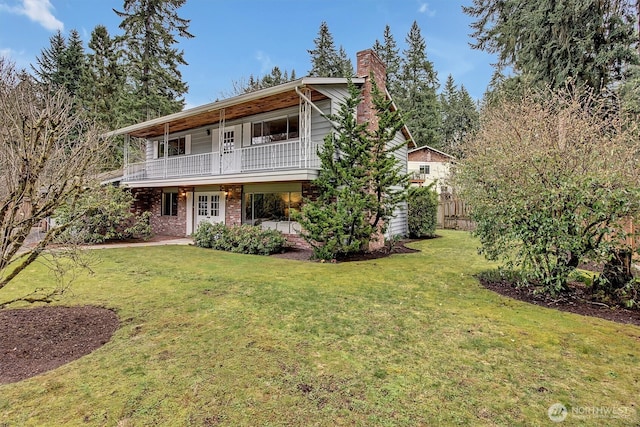 view of front property with a front yard, a balcony, fence, a chimney, and brick siding