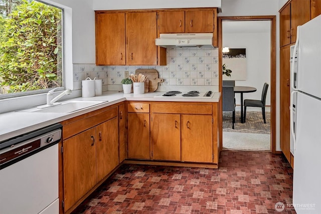 kitchen featuring white appliances, a sink, decorative backsplash, light countertops, and under cabinet range hood