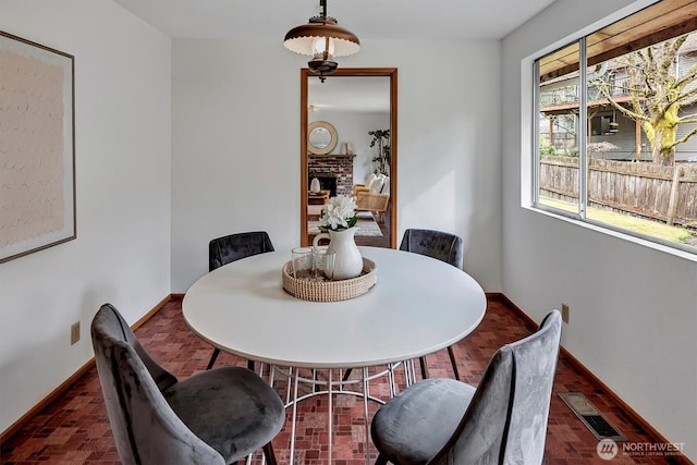 dining area featuring brick floor, visible vents, baseboards, and a brick fireplace