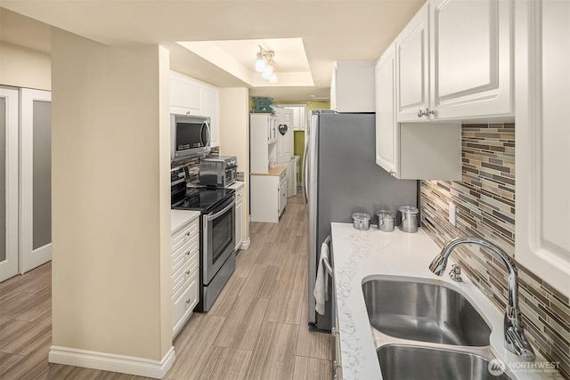 kitchen featuring stainless steel appliances, a sink, white cabinets, light countertops, and decorative backsplash