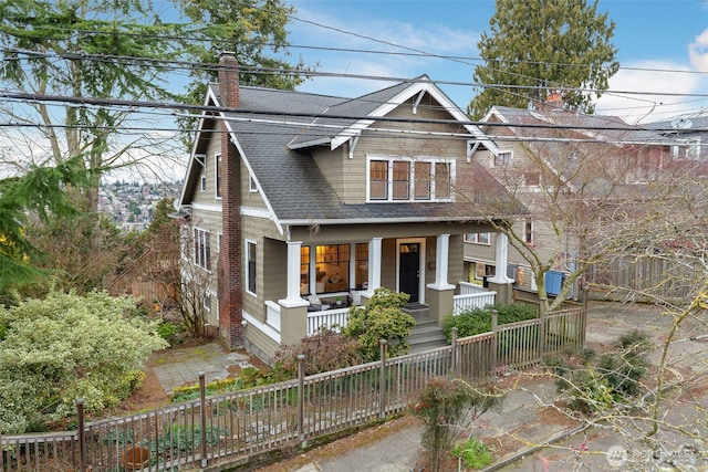 view of front of home featuring a porch, roof with shingles, a chimney, and a fenced front yard