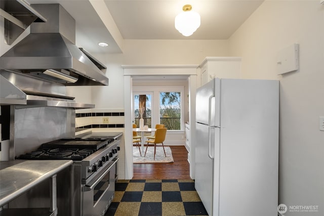 kitchen featuring dark floors, freestanding refrigerator, island exhaust hood, stainless steel stove, and backsplash