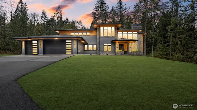 contemporary house with a lawn, an attached garage, a standing seam roof, stone siding, and driveway