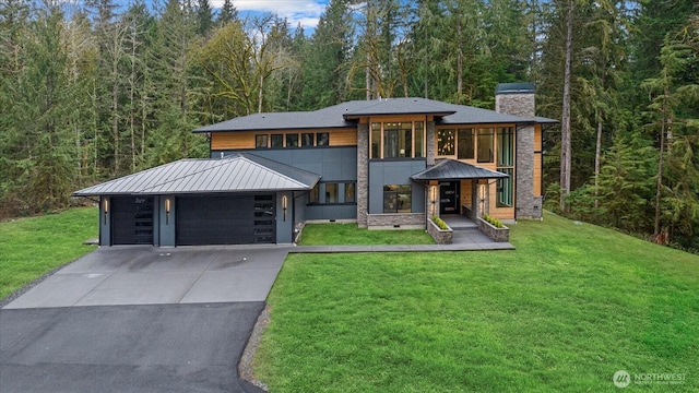 view of front of property featuring a standing seam roof, an attached garage, driveway, a chimney, and a front yard