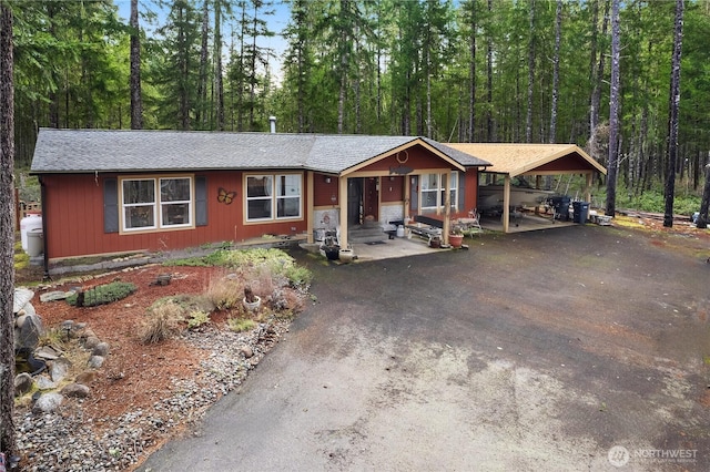 view of front facade with aphalt driveway, entry steps, a carport, and a forest view